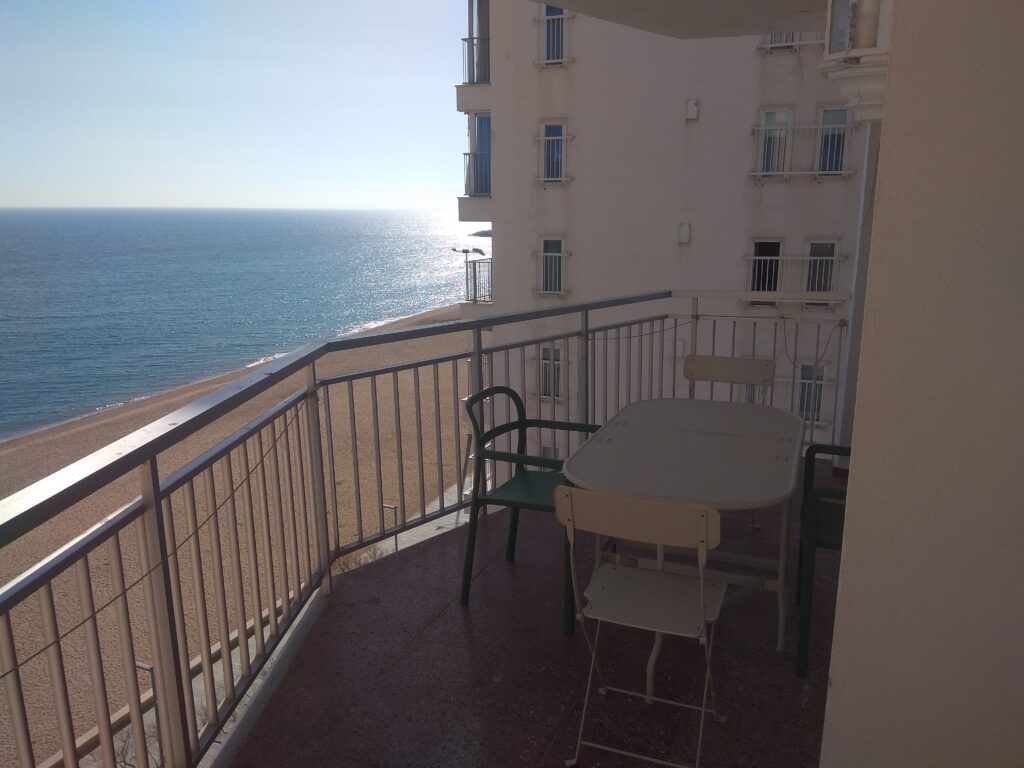 Vista de la terraza con mesa y cuatro sillas, a la izquierda la playa y a la derecha el edificio vecino.